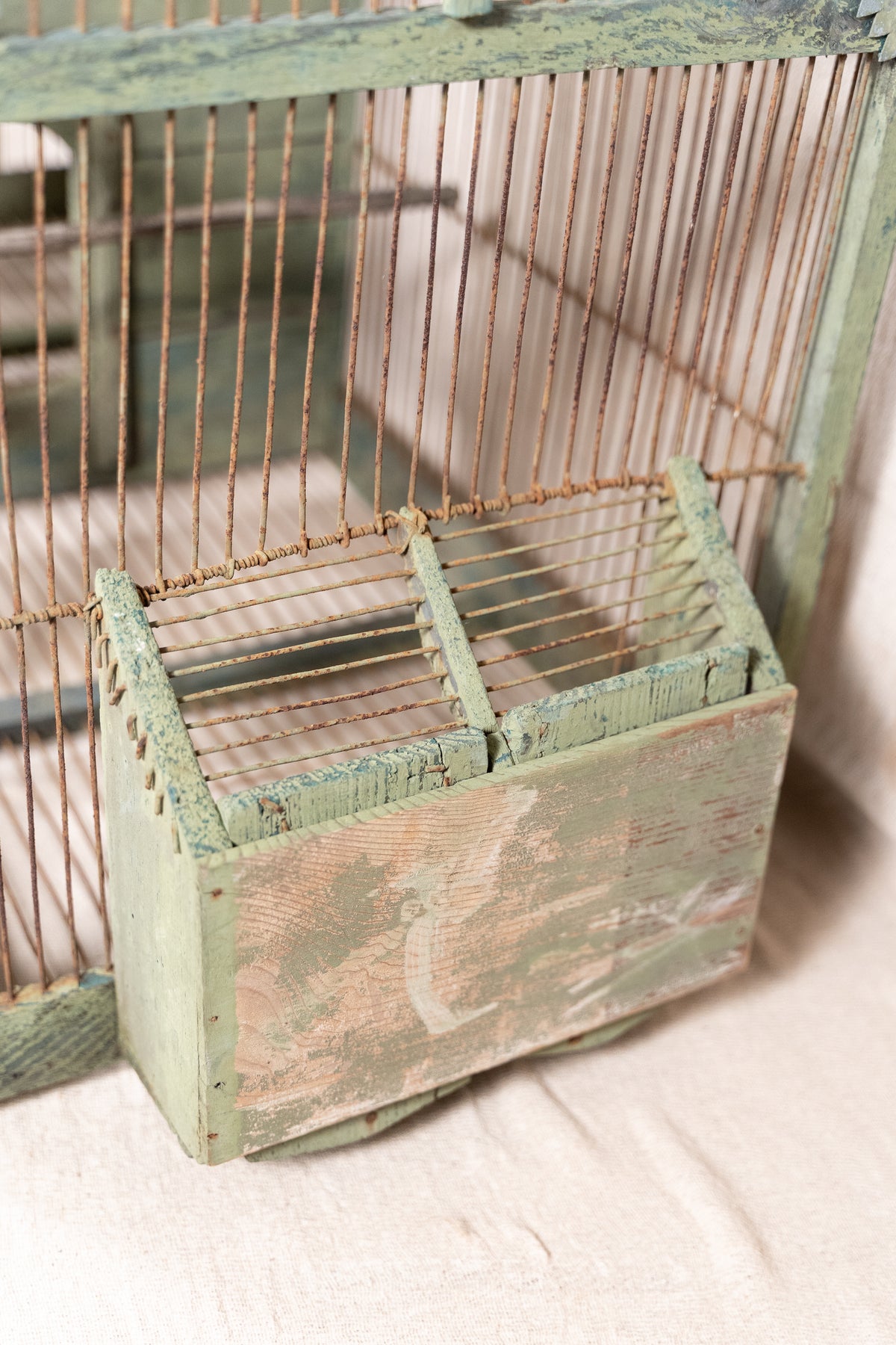 Vintage wooden birdcage with weathered green paint, decorative metal ridge detail, wire mesh panels and feeding troughs on both sides.