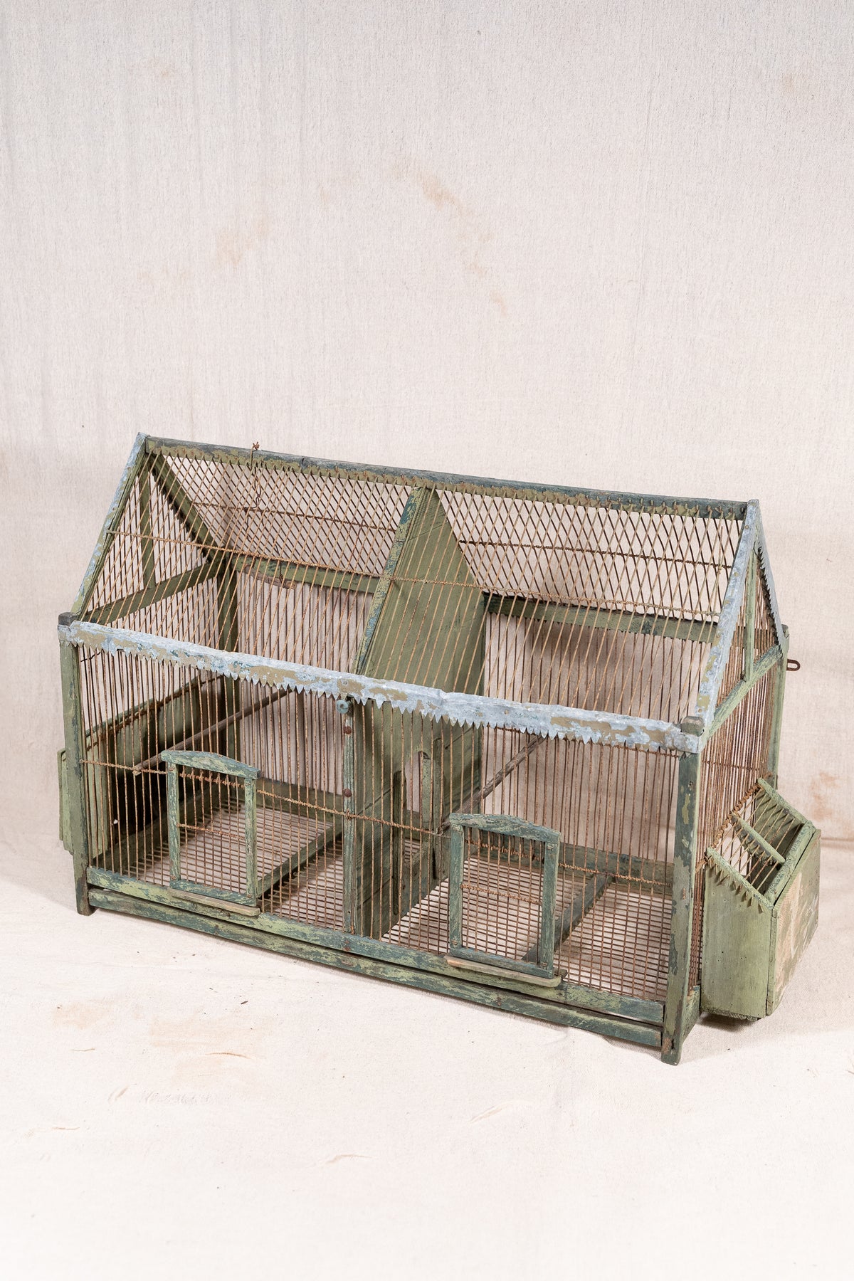 Vintage wooden birdcage with weathered green paint, decorative metal ridge detail, wire mesh panels and feeding troughs on both sides.