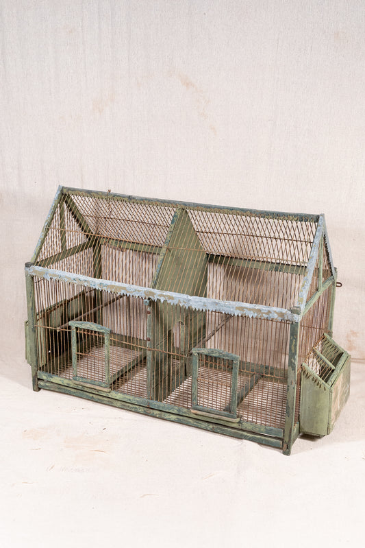 Vintage wooden birdcage with weathered green paint, decorative metal ridge detail, wire mesh panels and feeding troughs on both sides.