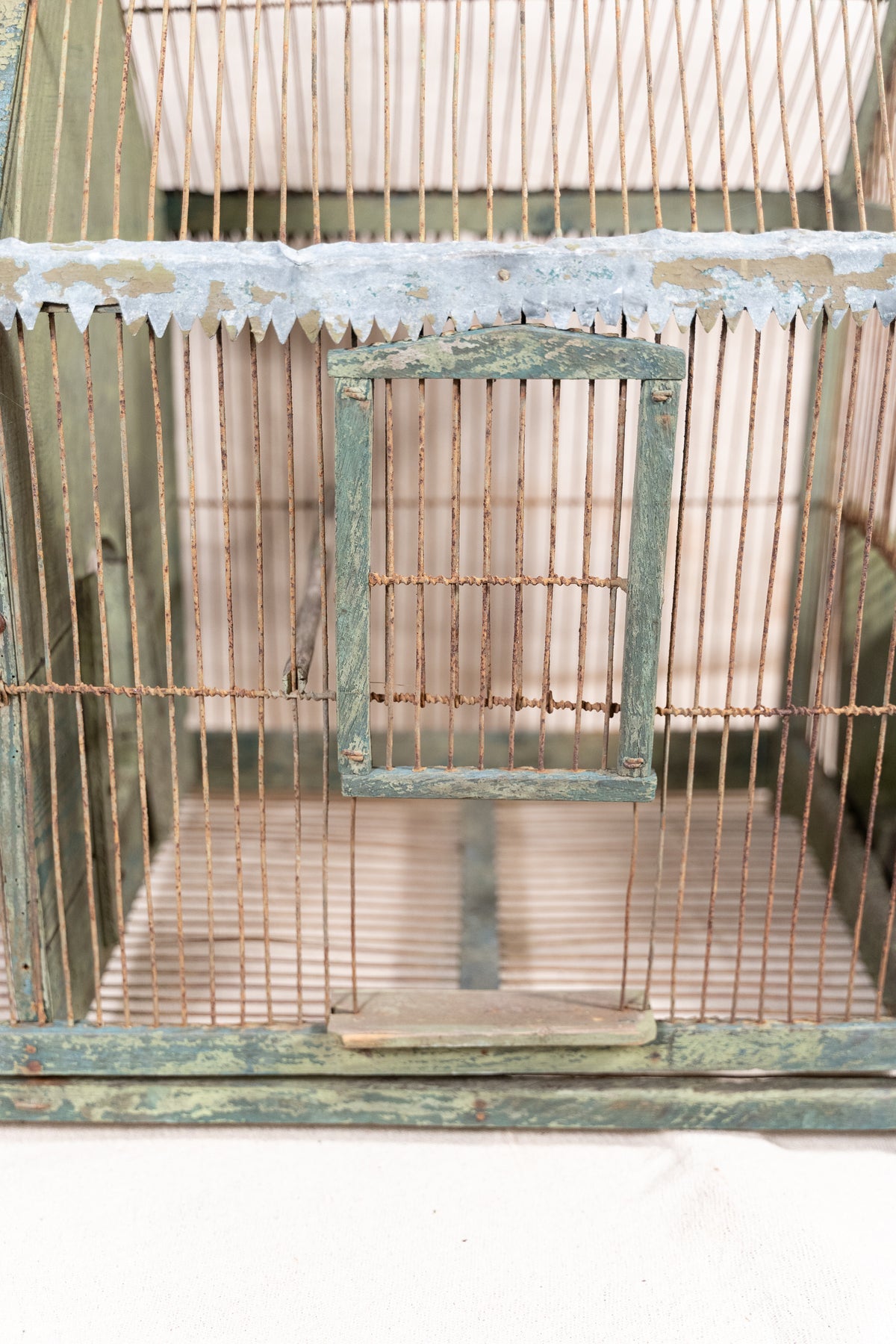 Vintage wooden birdcage with weathered green paint, decorative metal ridge detail, wire mesh panels and feeding troughs on both sides.
