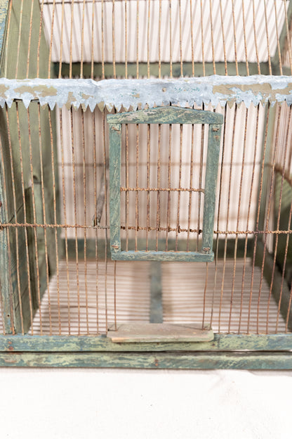 Vintage wooden birdcage with weathered green paint, decorative metal ridge detail, wire mesh panels and feeding troughs on both sides.