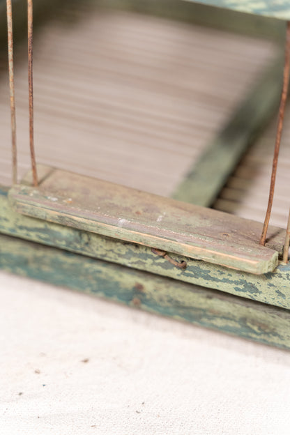 Vintage wooden birdcage with weathered green paint, decorative metal ridge detail, wire mesh panels and feeding troughs on both sides.