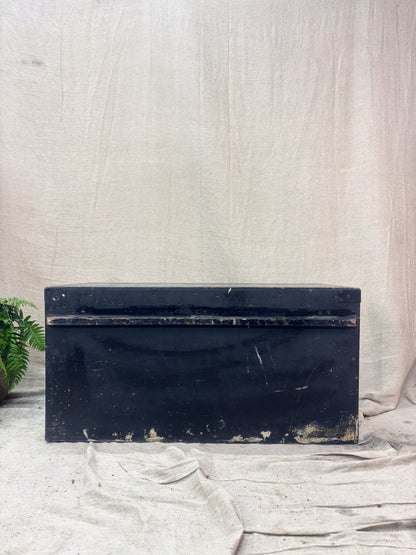 Black rectangular trunk on a textured white surface with a plant in the corner