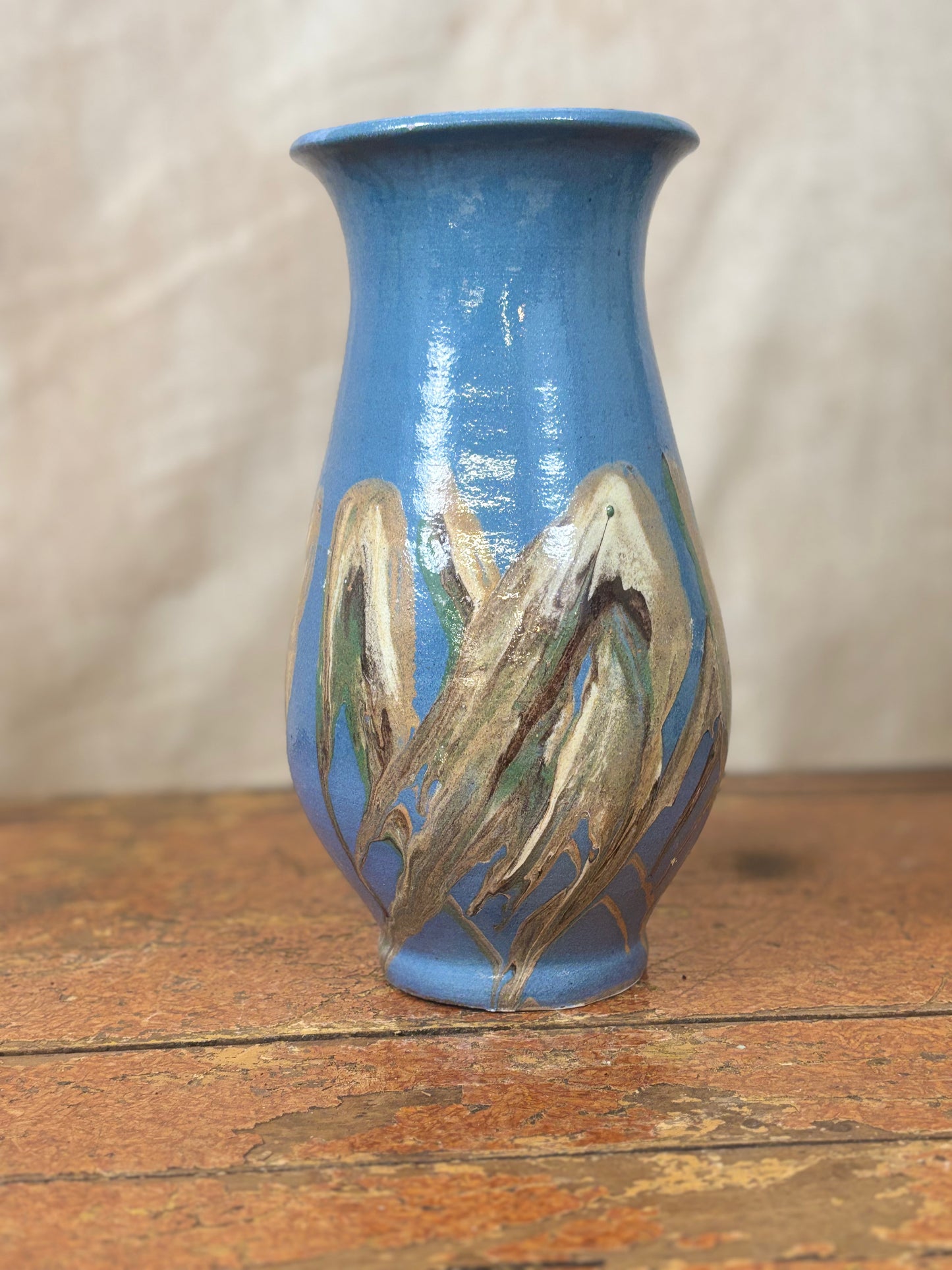 Blue ceramic vase with artistic brown designs on a wooden surface
