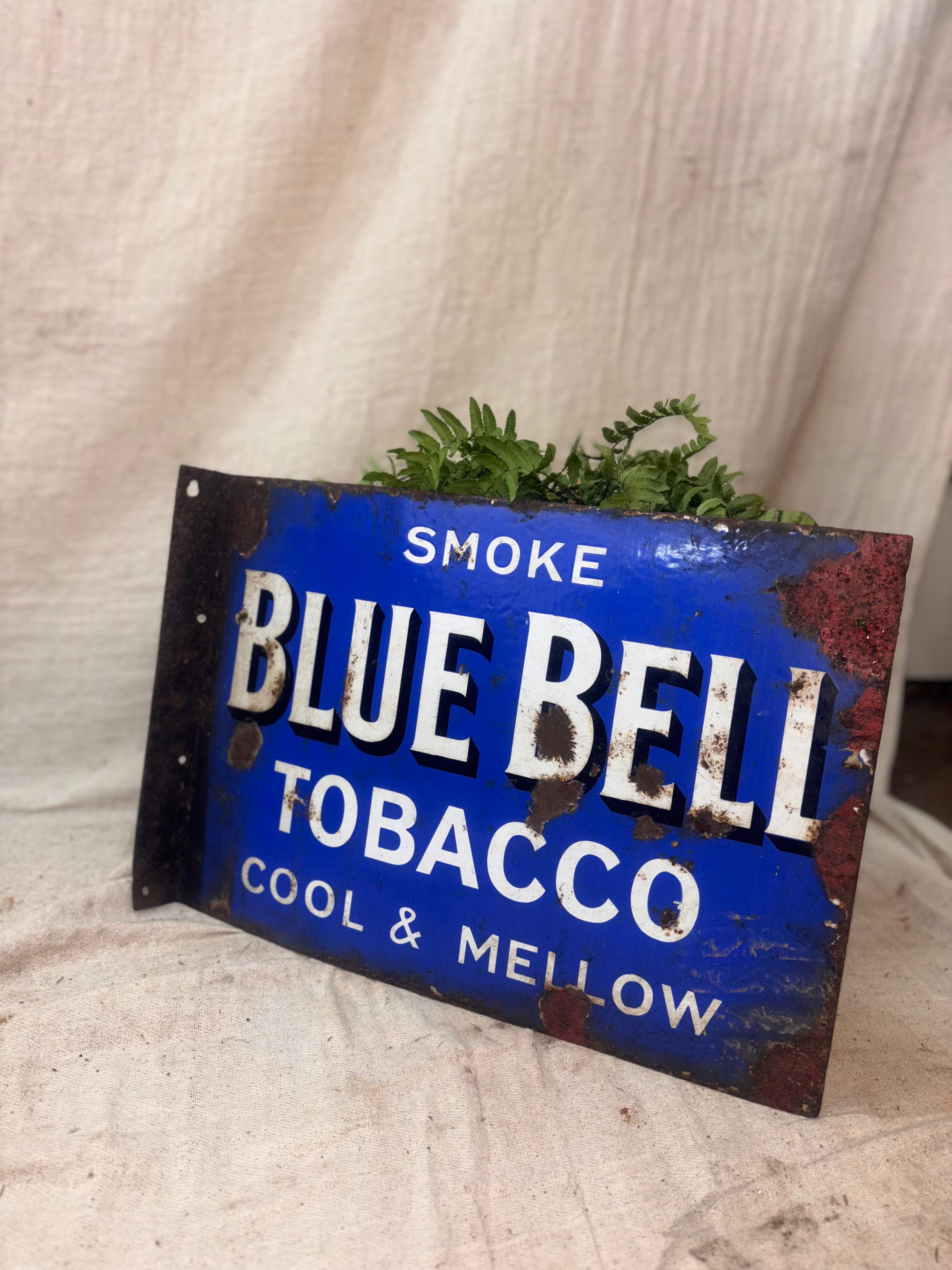 Vintage Blue Bell Tobacco sign with plants on a textured surface