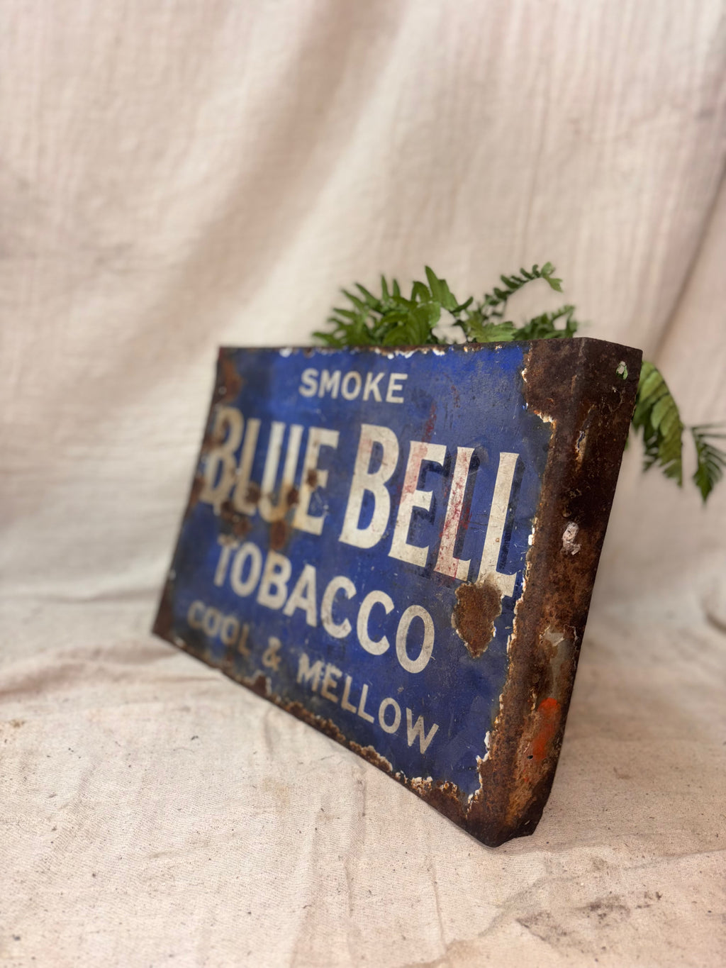 Vintage Blue Bell Tobacco sign with rust and wear on a textured fabric background