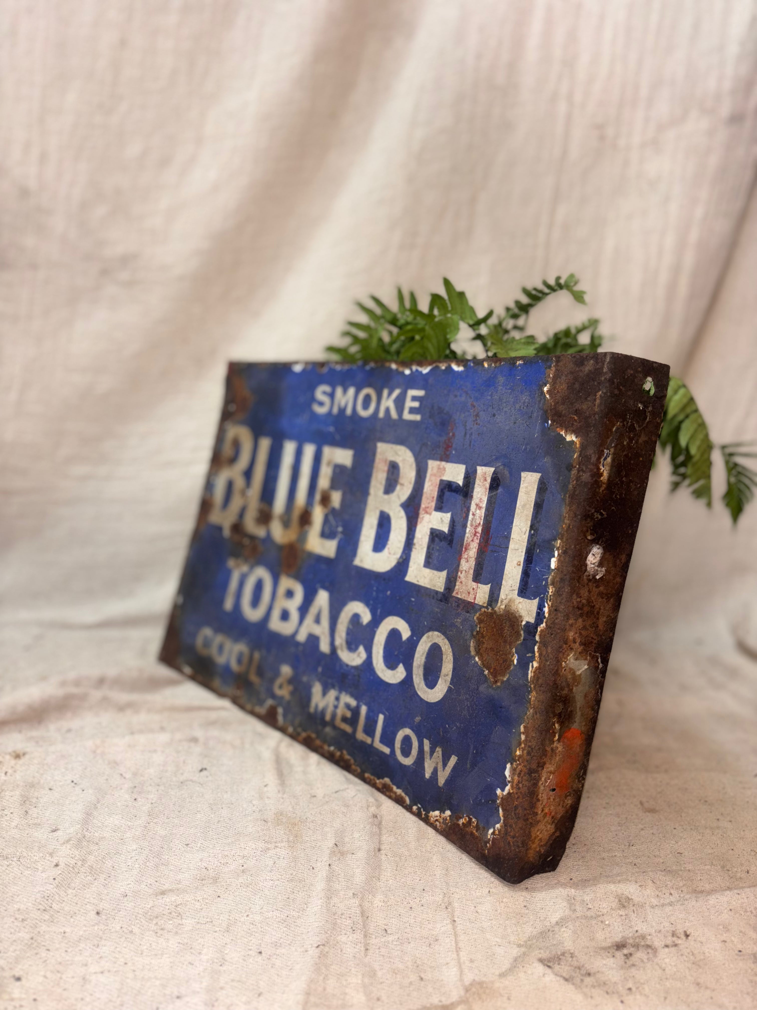 Vintage Blue Bell Tobacco sign with rust and wear on a textured fabric background