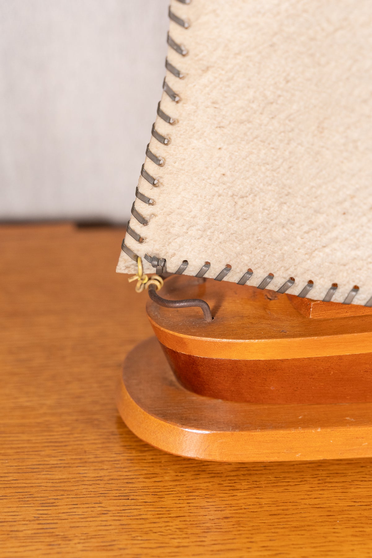 Close-up of a wooden model sailboat or decorative boat stand with a beige sail and metal rigging on a wooden tabletop.