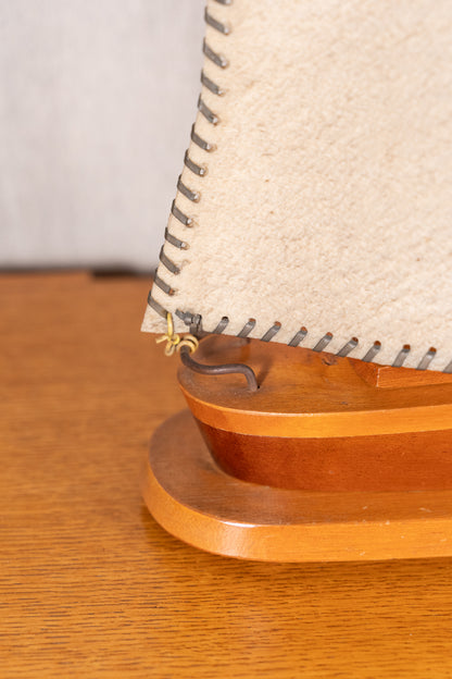 Close-up of a wooden model sailboat or decorative boat stand with a beige sail and metal rigging on a wooden tabletop.