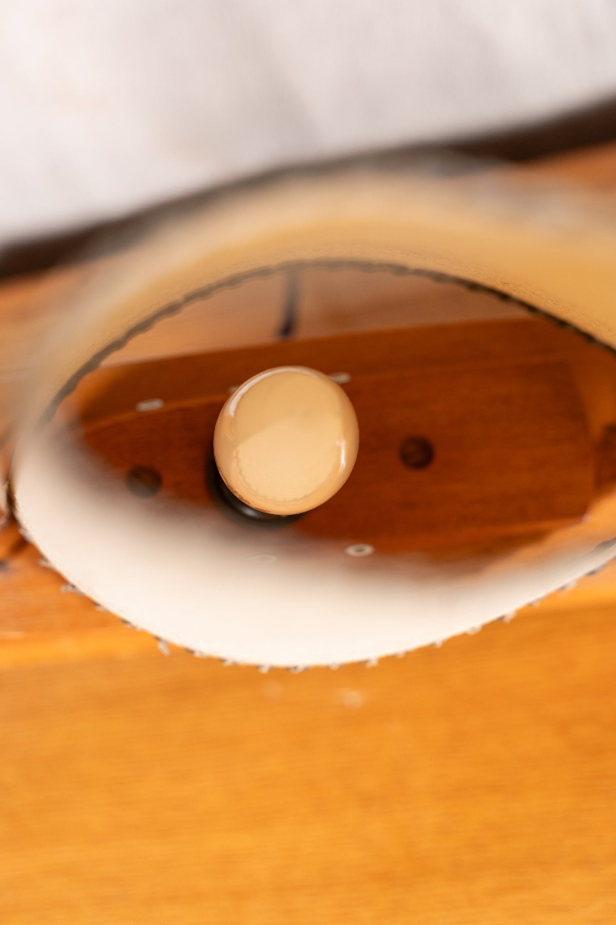 Close-up of a polished wooden object with a circular beige knob or button, showing warm brown wood tones and a white curved edge.