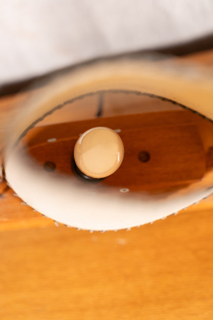 Close-up of a polished wooden object with a circular beige knob or button, showing warm brown wood tones and a white curved edge.