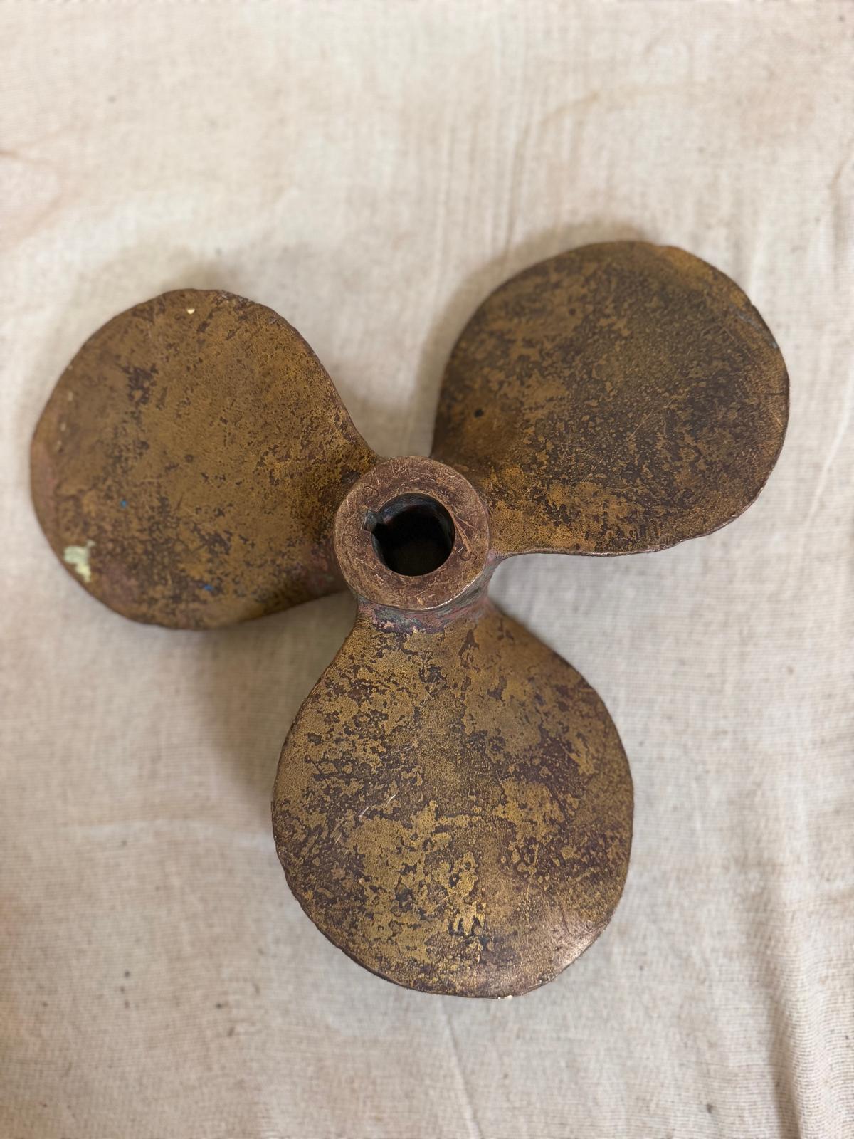 Rust-covered three-blade propeller on a beige fabric background