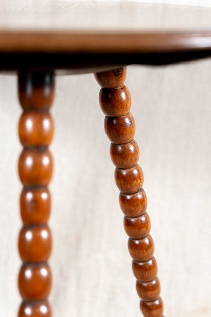 Close-up of a wooden table leg with a distinctive beaded spindle design, showing warm medium-brown wood grain against a light neutral background.