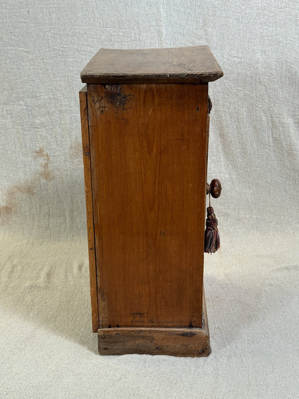 Wooden bedside cabinet with patterned fabric-inset door, braided gimp trim, tassel knob and carved egg-and-dart detailing. 