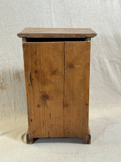Wooden bedside cabinet with patterned fabric-inset door, braided gimp trim, tassel knob and carved egg-and-dart detailing. 