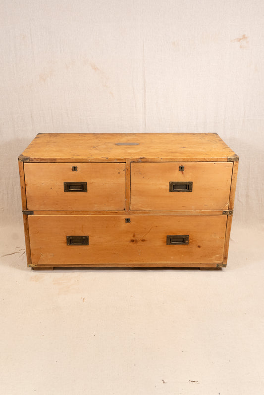 A vintage wooden storage chest with four drawers, featuring a light natural wood finish and dark metal drawer pulls, set against a plain off-white background.