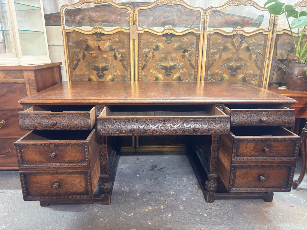 Vintage wooden desk with intricate carvings and multiple drawers in a room setting.