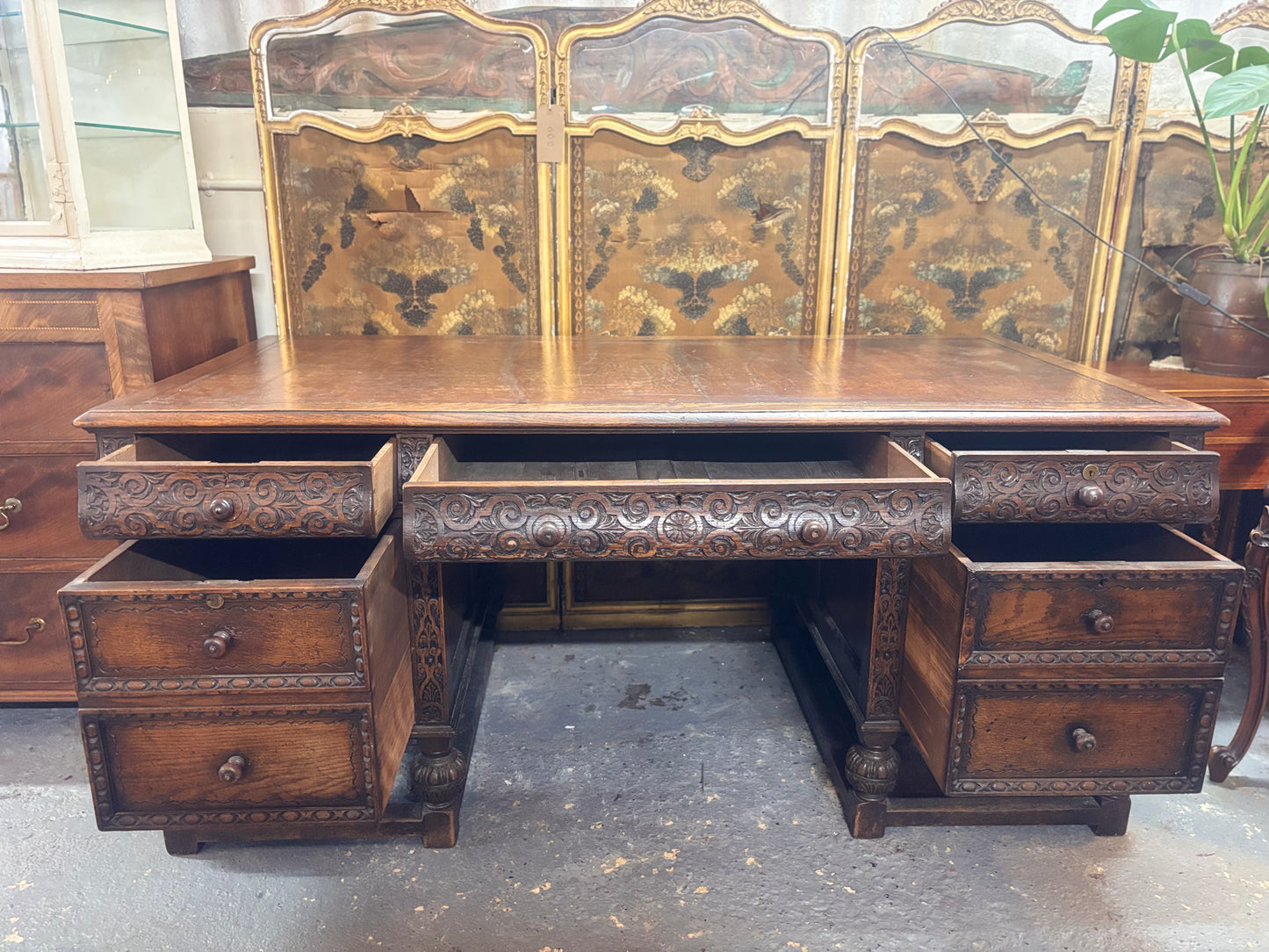 Vintage wooden desk with intricate carvings and multiple drawers in a room setting.