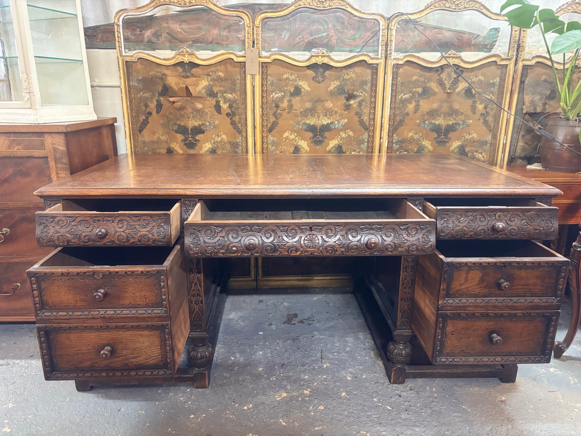 Vintage wooden desk with intricate carvings and multiple drawers in a room setting.