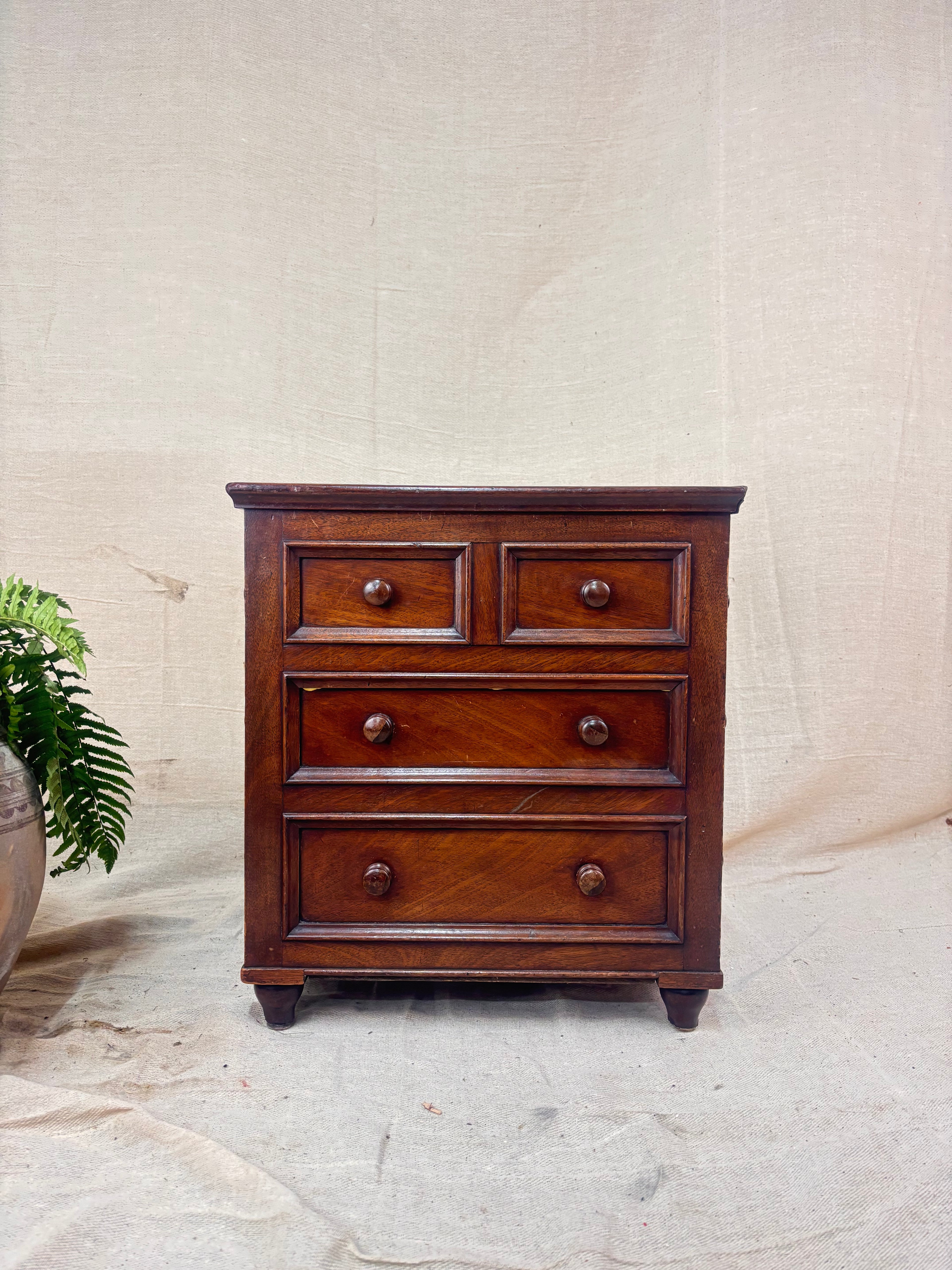 Wooden dresser with four drawers on a stone floor against a beige wall.