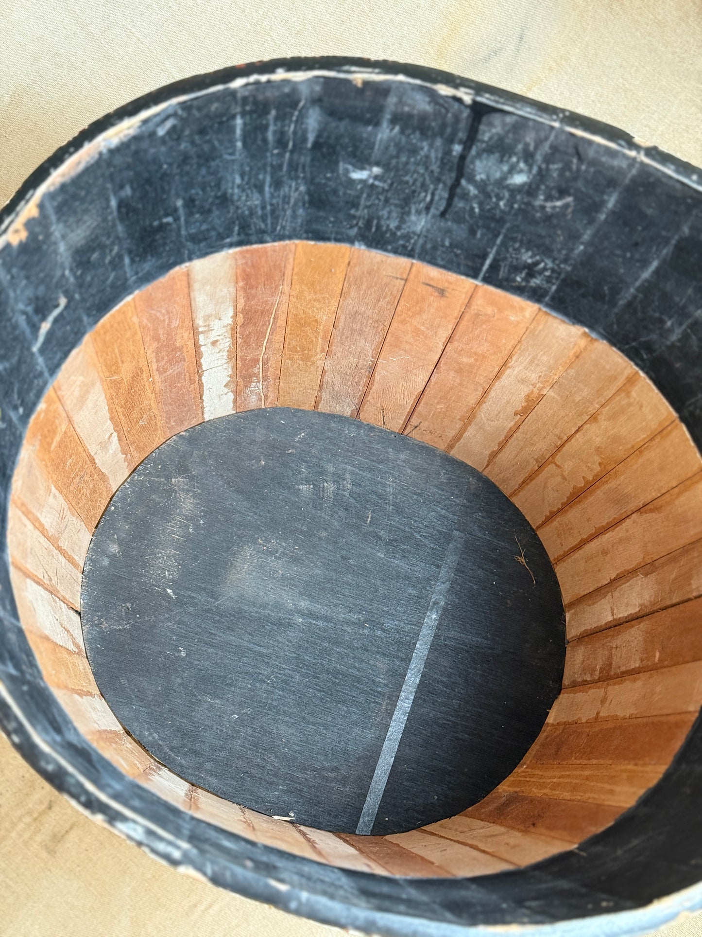 Close-up of the inside of a bucket or barrel, showing a black outer rim, a light brown wooden slatted interior, and a dark circular bottom plate.