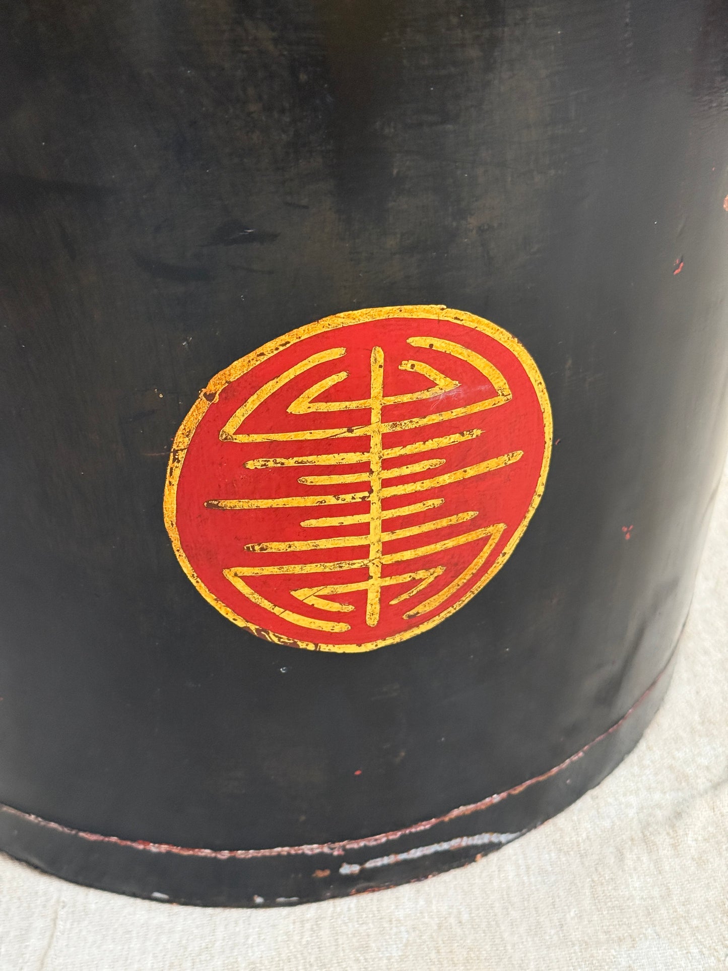 Close-up of a black cylindrical object with a circular red and gold emblem on the side, photographed against a light fabric background.