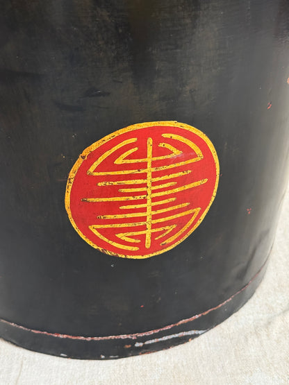 Close-up of a black cylindrical object with a circular red and gold emblem on the side, photographed against a light fabric background.