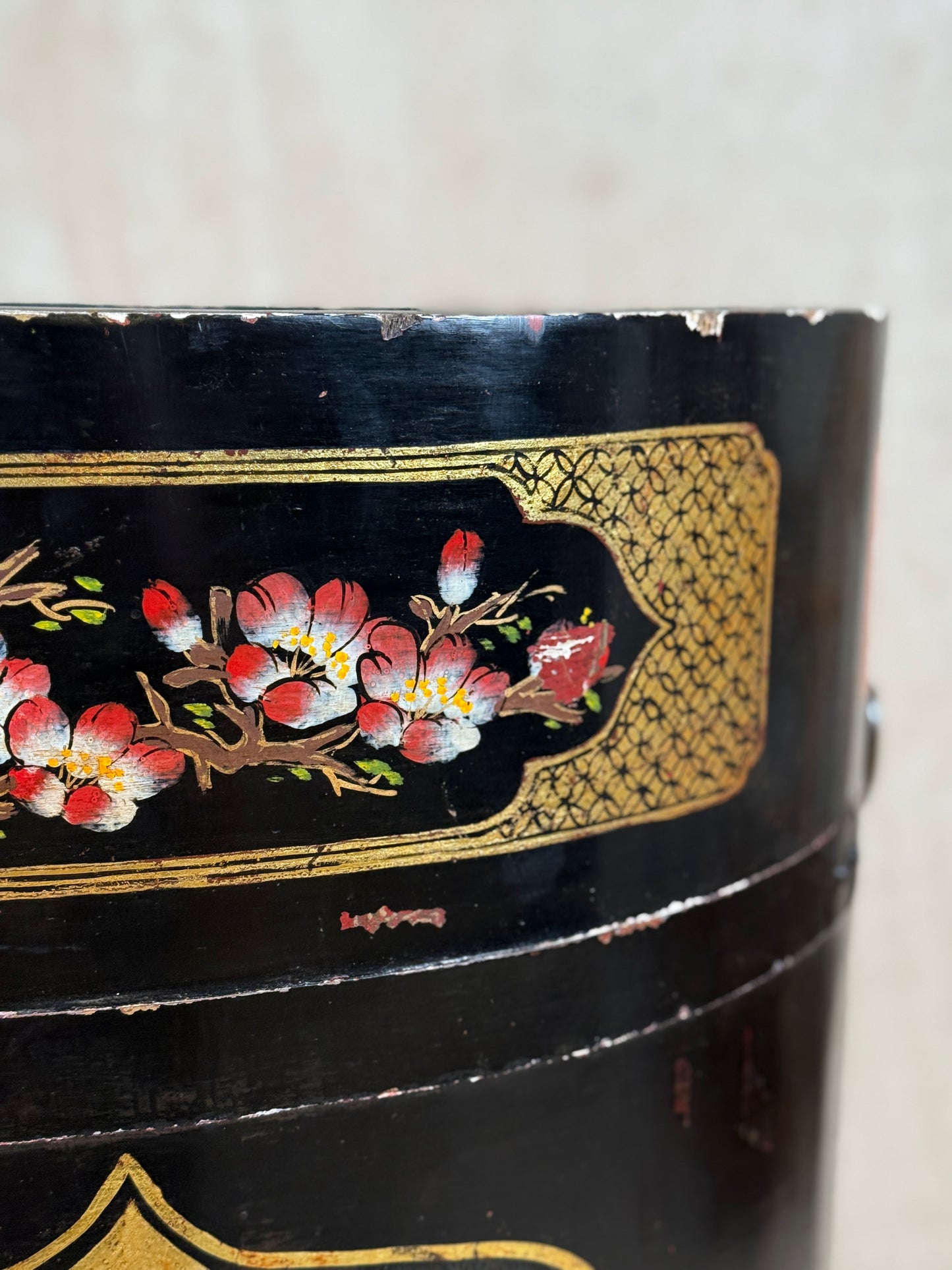 Close-up of a black cylindrical decorative container or box with hand-painted red, white, and yellow floral blossoms and gold ornamental detailing.