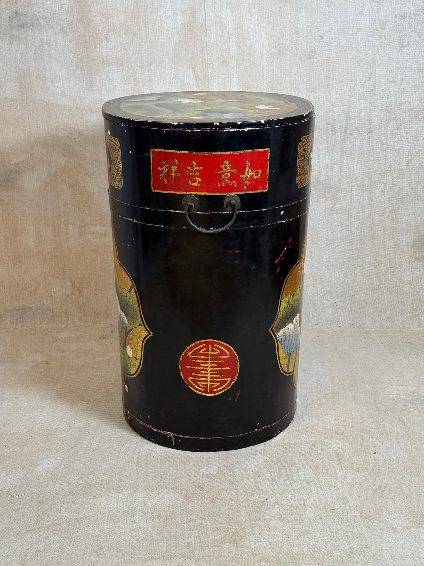 A vintage black lacquered cylindrical storage box or tea canister with hand-painted gold, red, and green decorative motifs, featuring a red label with gold Chinese characters and a metal handle.