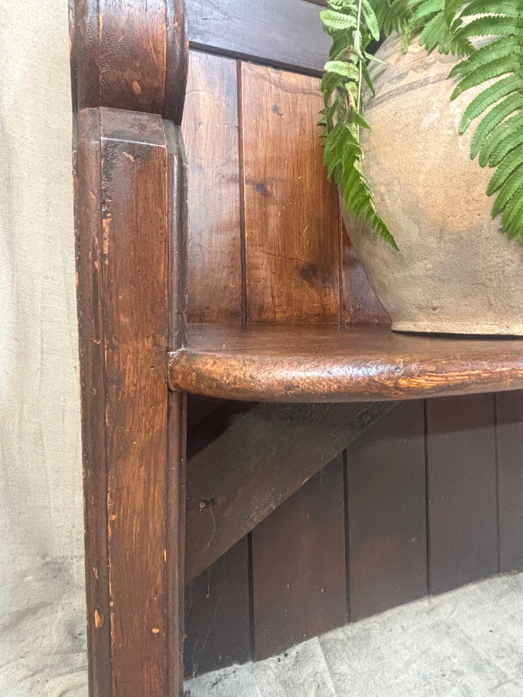 Wooden bench with a textured surface and a plant in the background