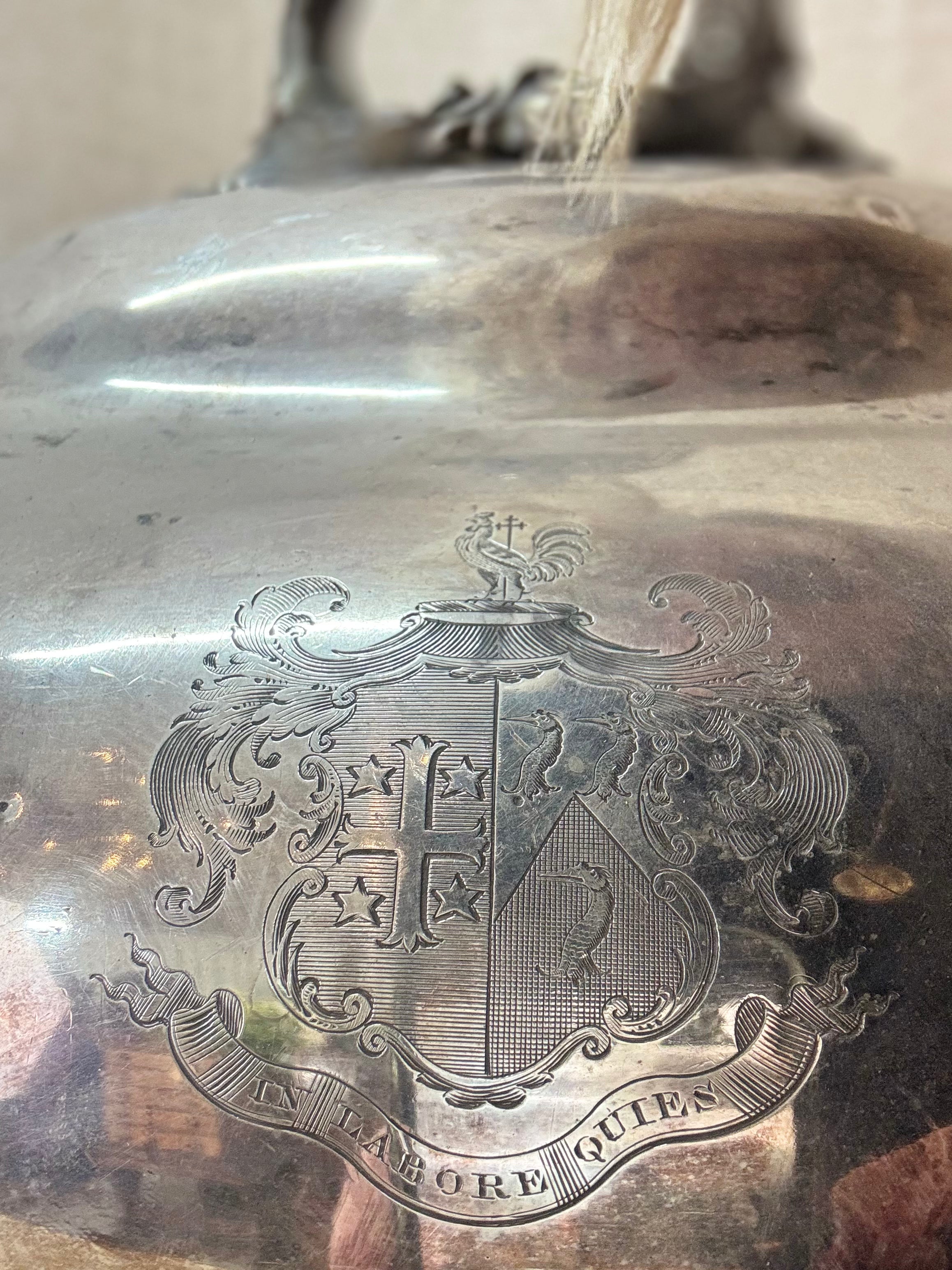 Close-up of a silver meat cover with engraved design and 'In labōre quiēs' text.