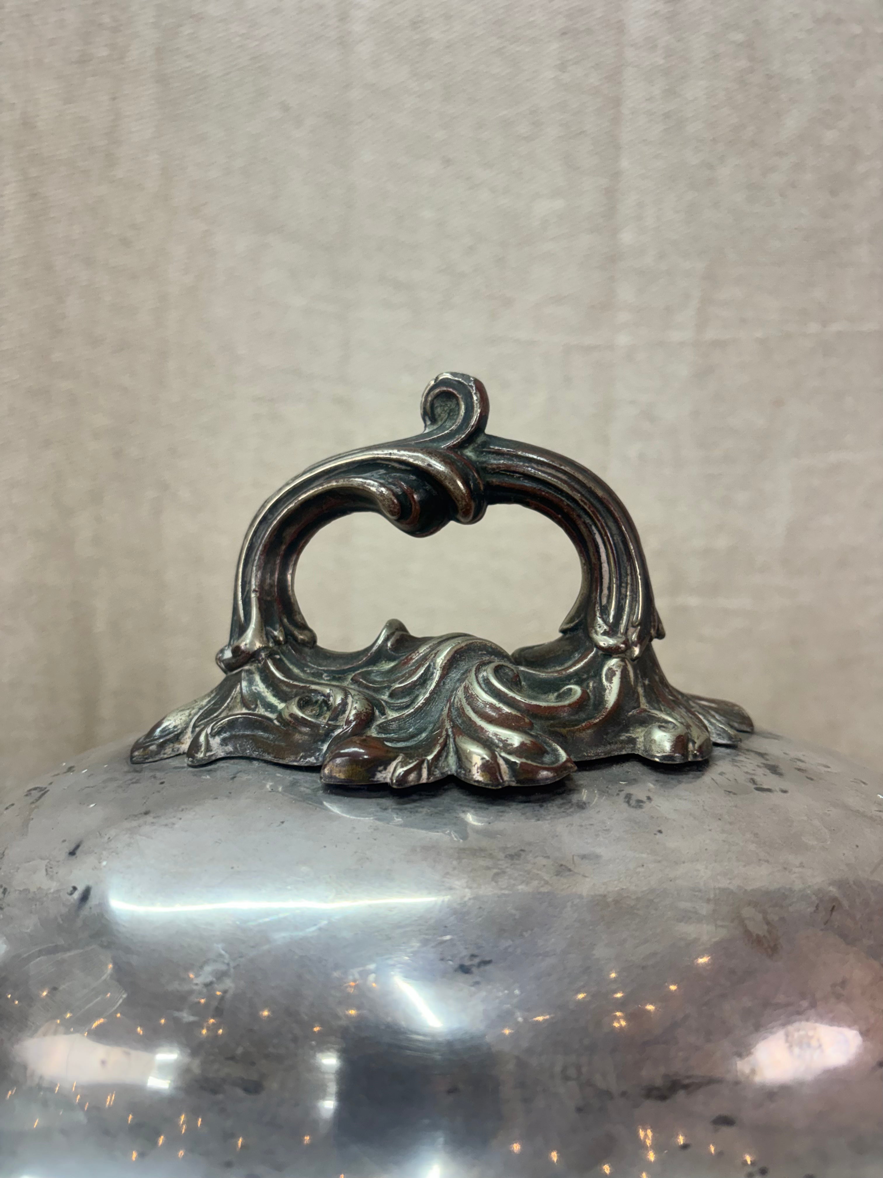 Decorative metal lid with intricate handle on a plain background