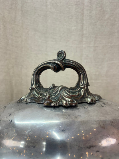 Decorative metal lid with intricate handle on a plain background