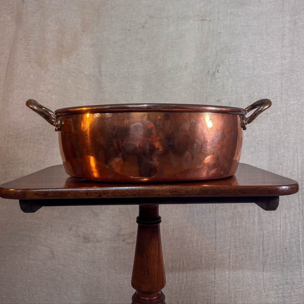 Copper pot on a wooden stand against a textured wall