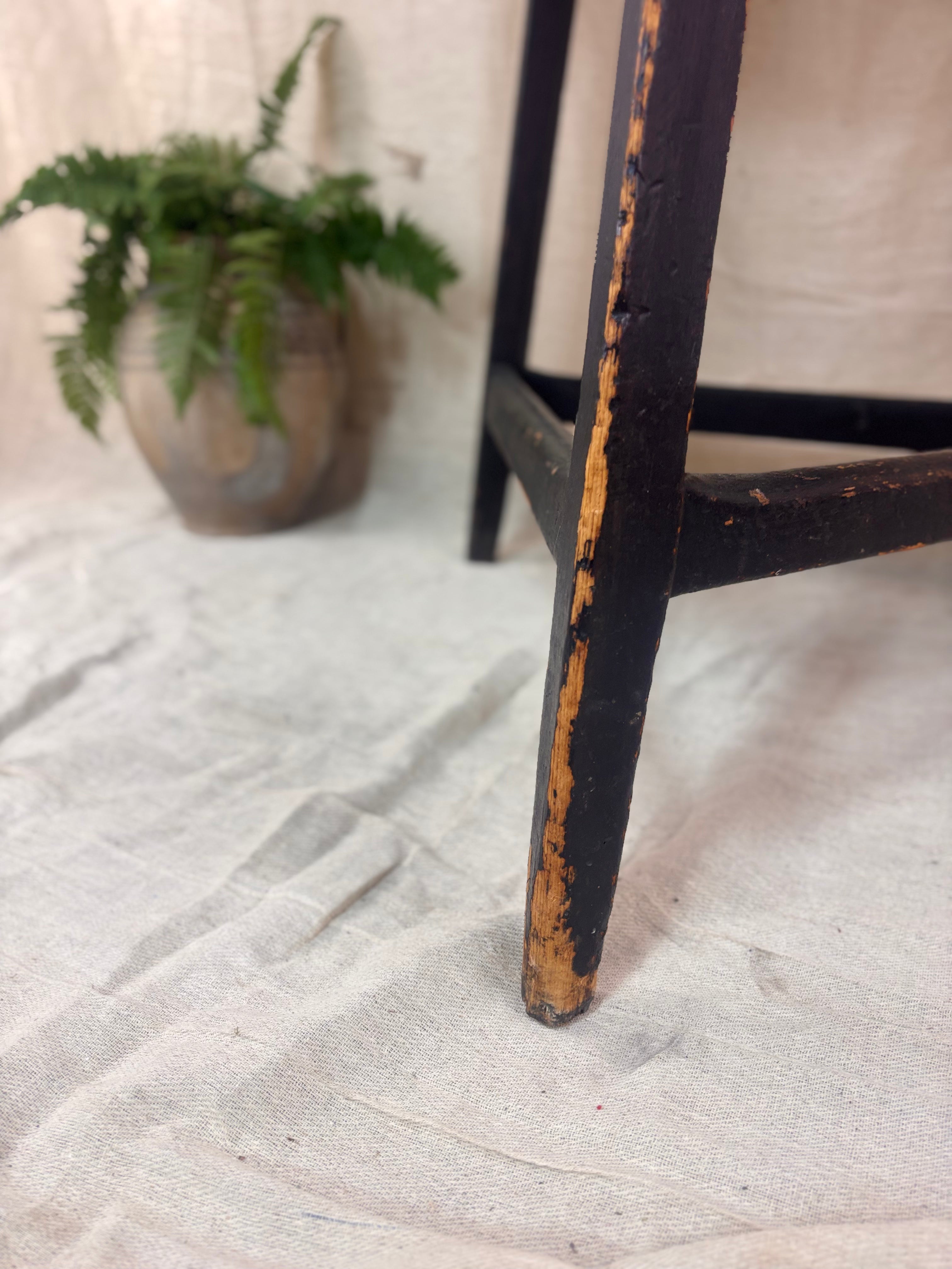 Worn black table leg on a textured surface with a plant in the background