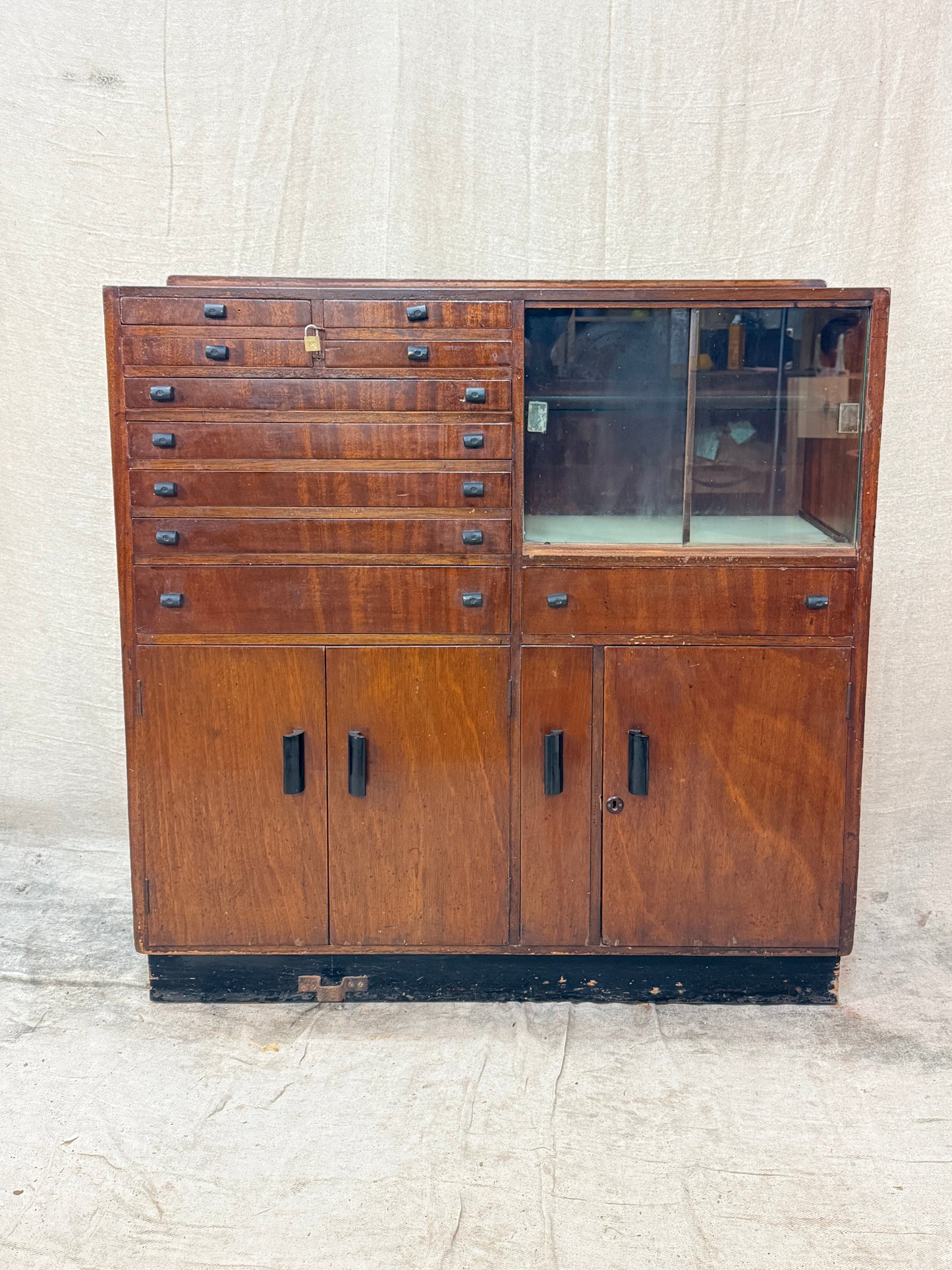 Wooden cabinet with glass door and drawers on a textured white wall.