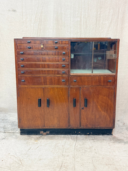 Wooden cabinet with glass door and drawers on a textured white wall.