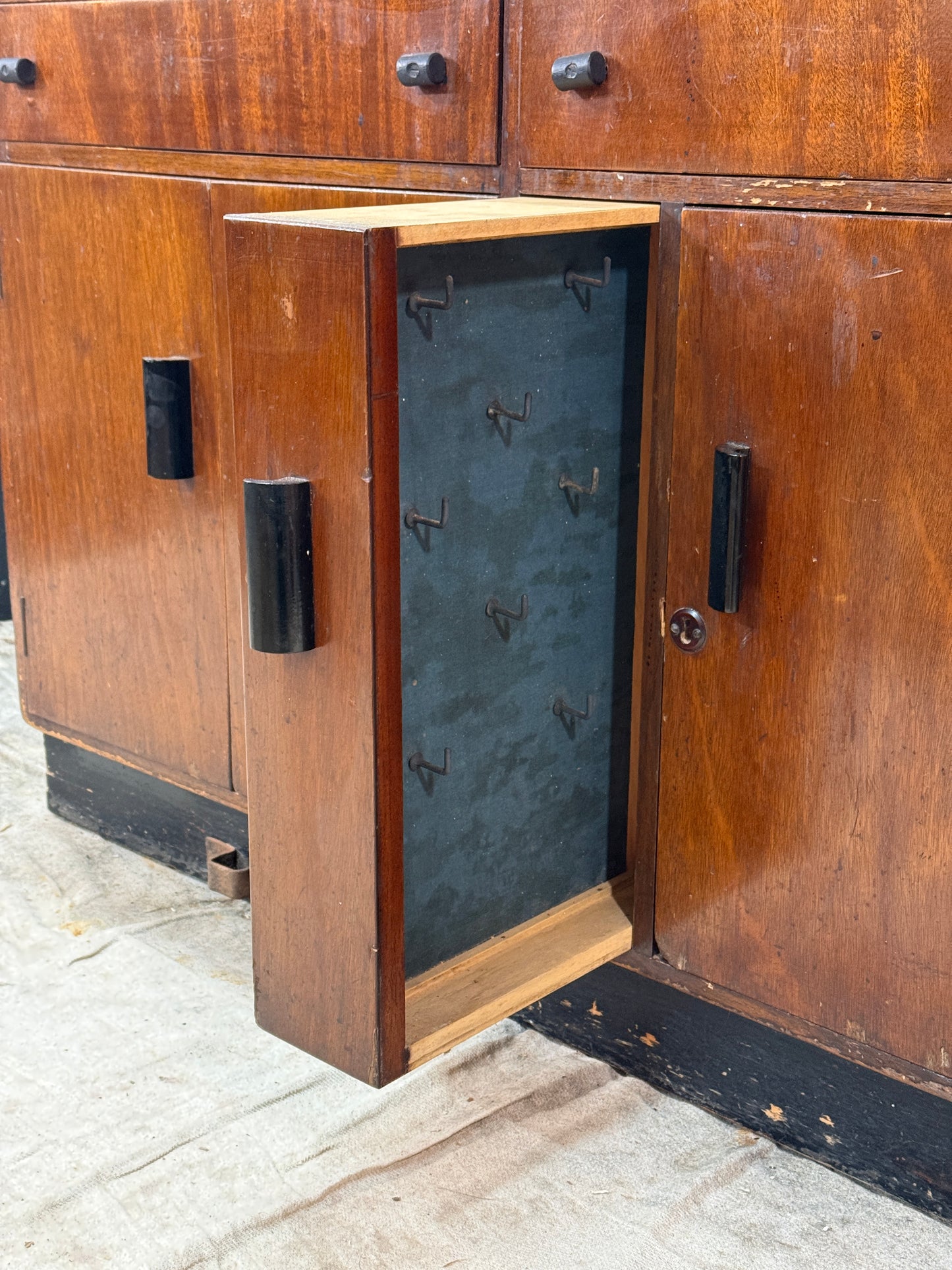 Wooden cabinet with open drawer showing metal objects on a concrete floor.