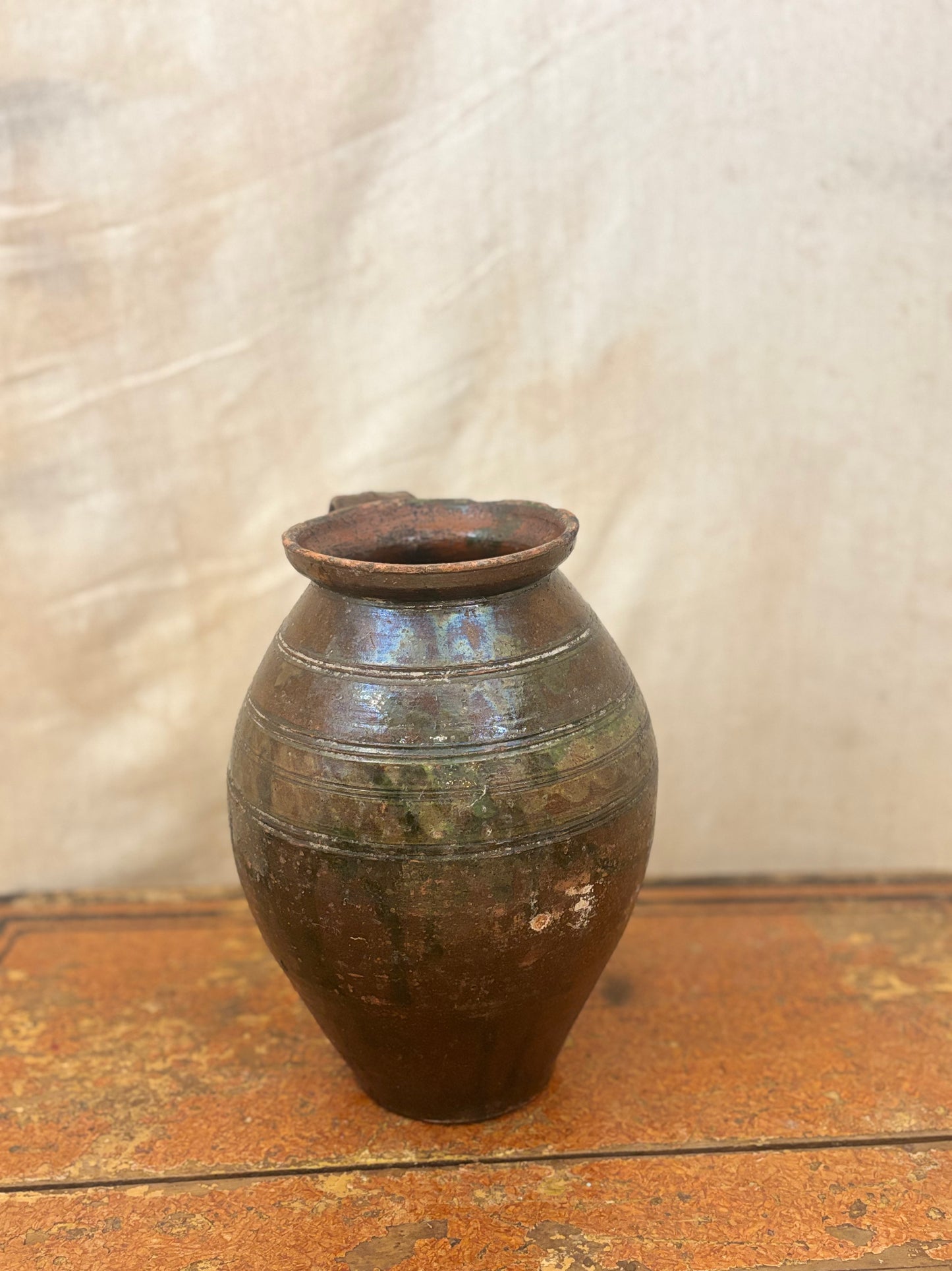 Brown ceramic vase on a wooden surface with a textured white background