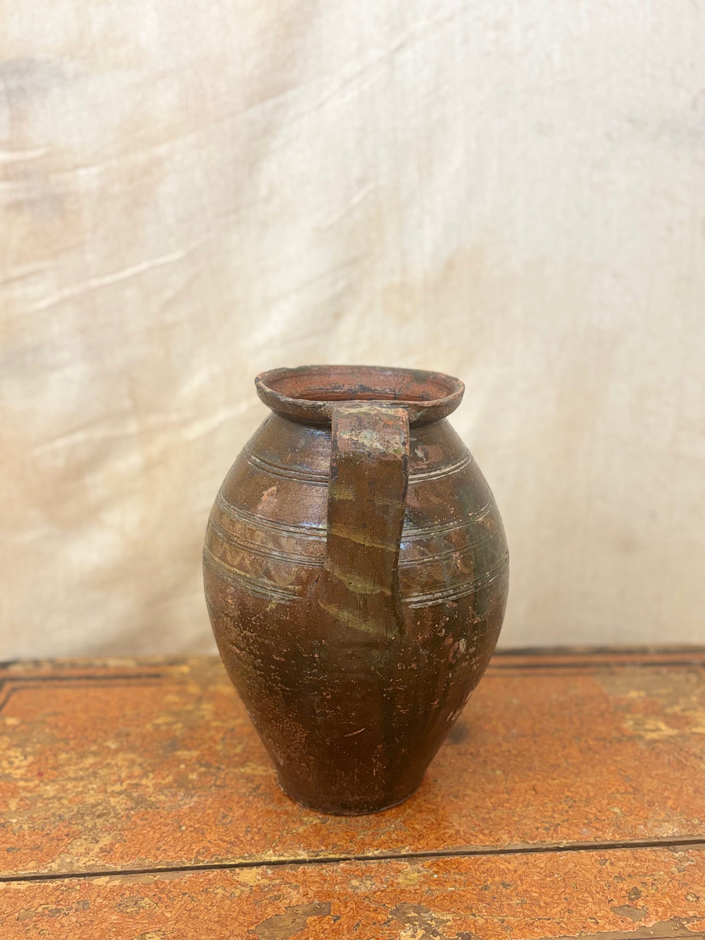 Brown ceramic pitcher on a wooden surface with a textured white background