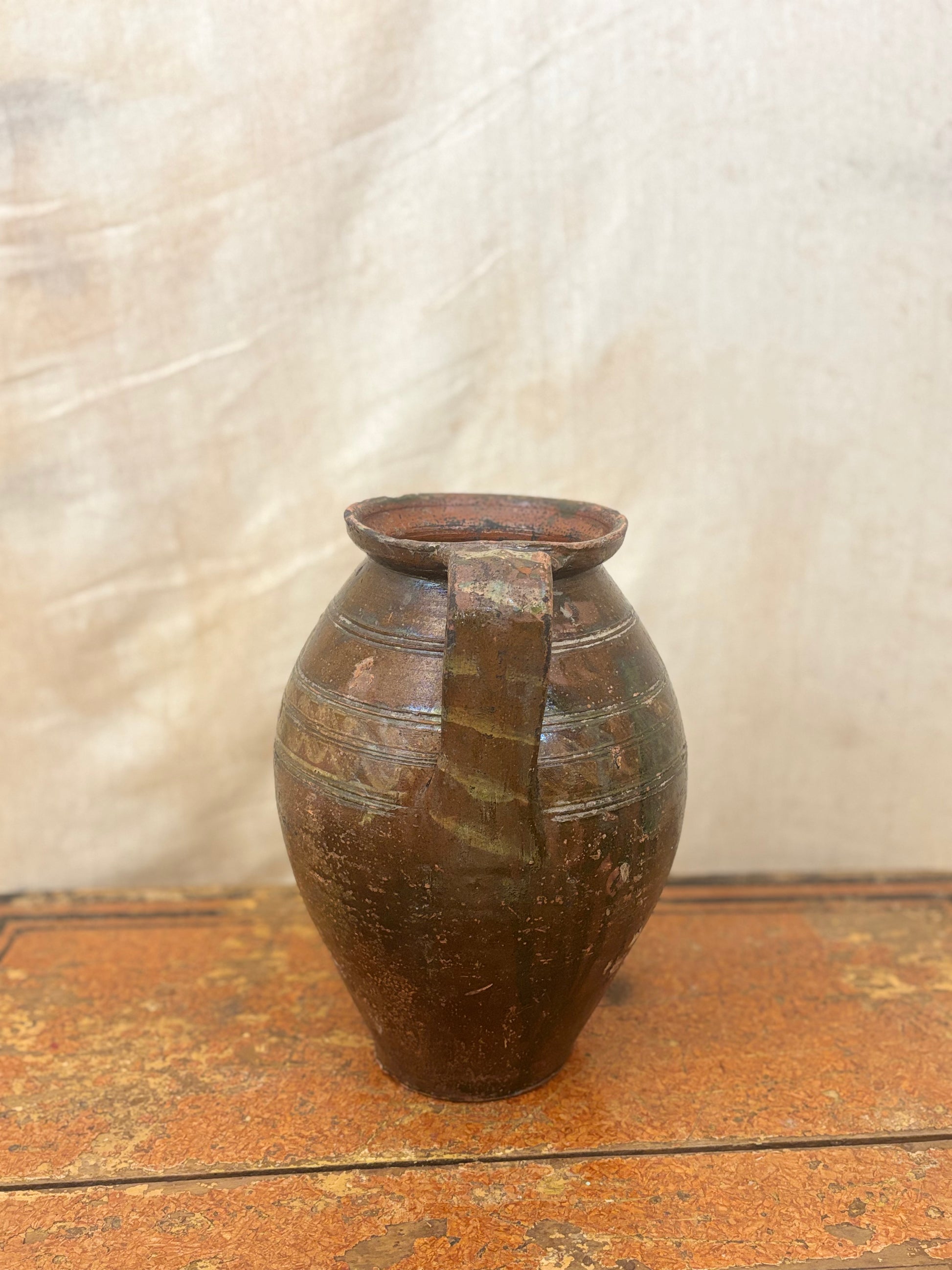 Brown ceramic pitcher on a wooden surface with a textured white background