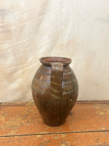 Brown ceramic pitcher on a wooden surface with a textured white background