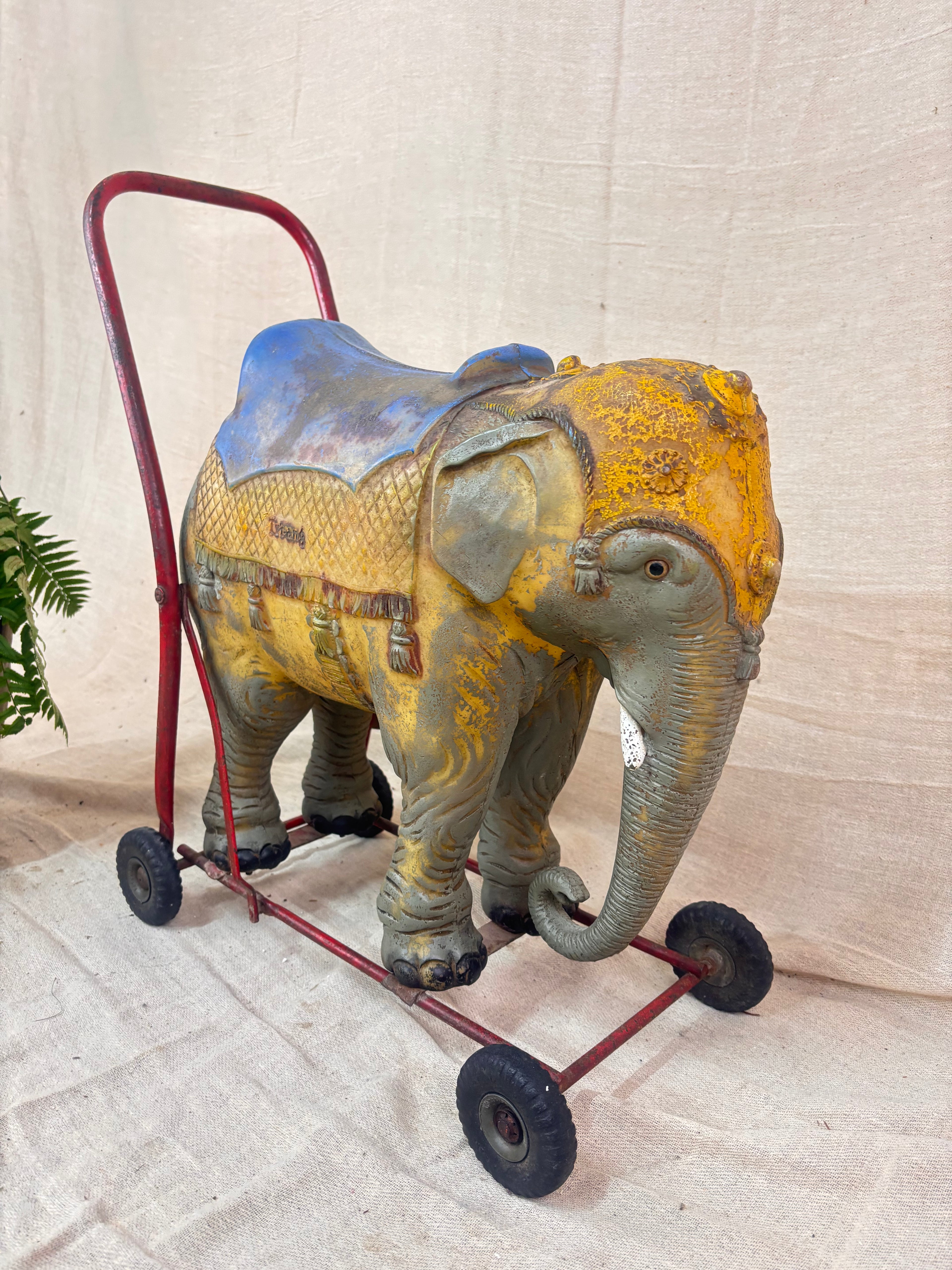 Vintage 1950s Tri-ang push-along elephant toy with hard plastic body, blue saddle, and red metal chassis with rubber wheels