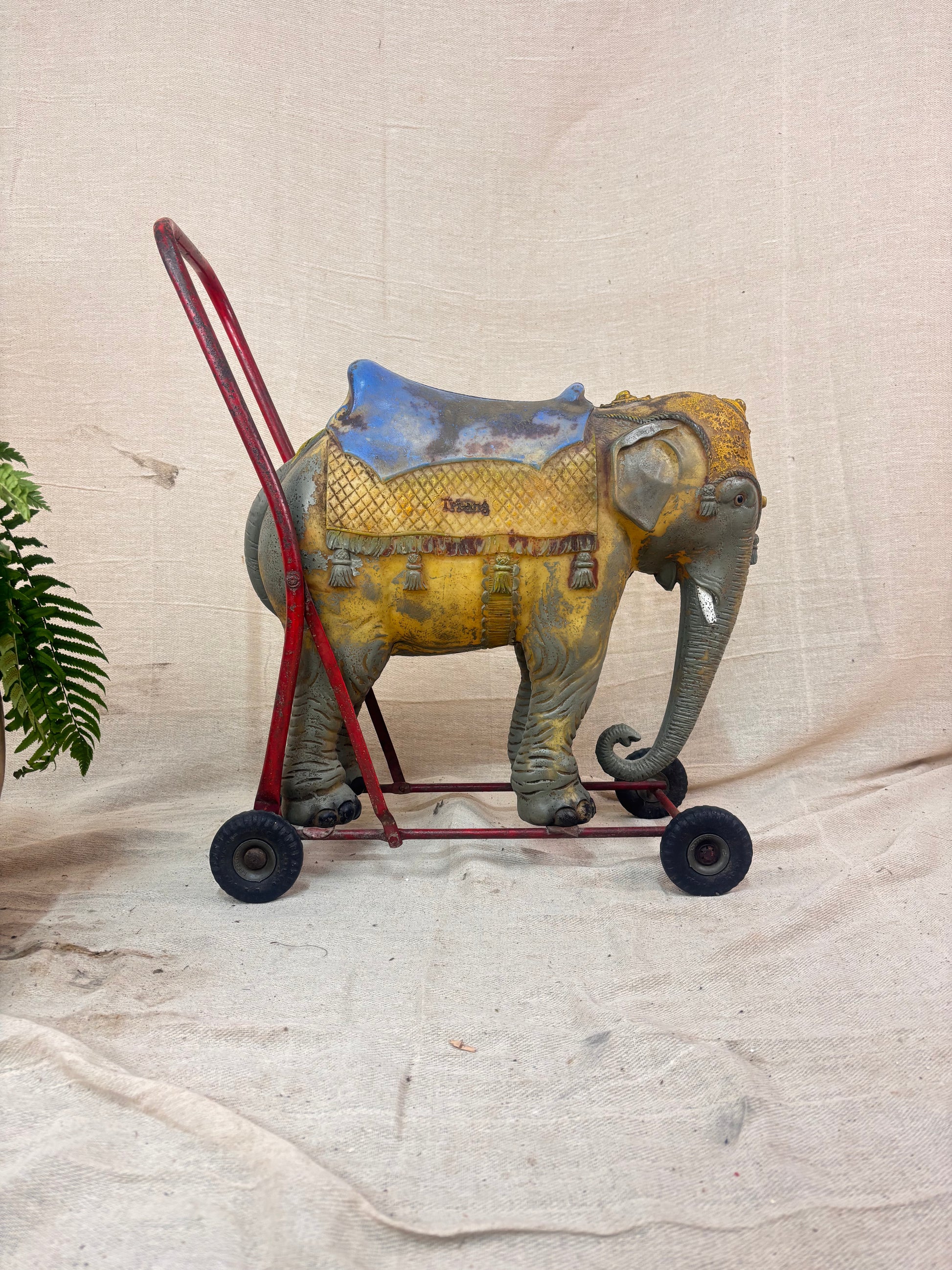 Vintage 1950s Tri-ang push-along elephant toy with hard plastic body, blue saddle, and red metal chassis with rubber wheels