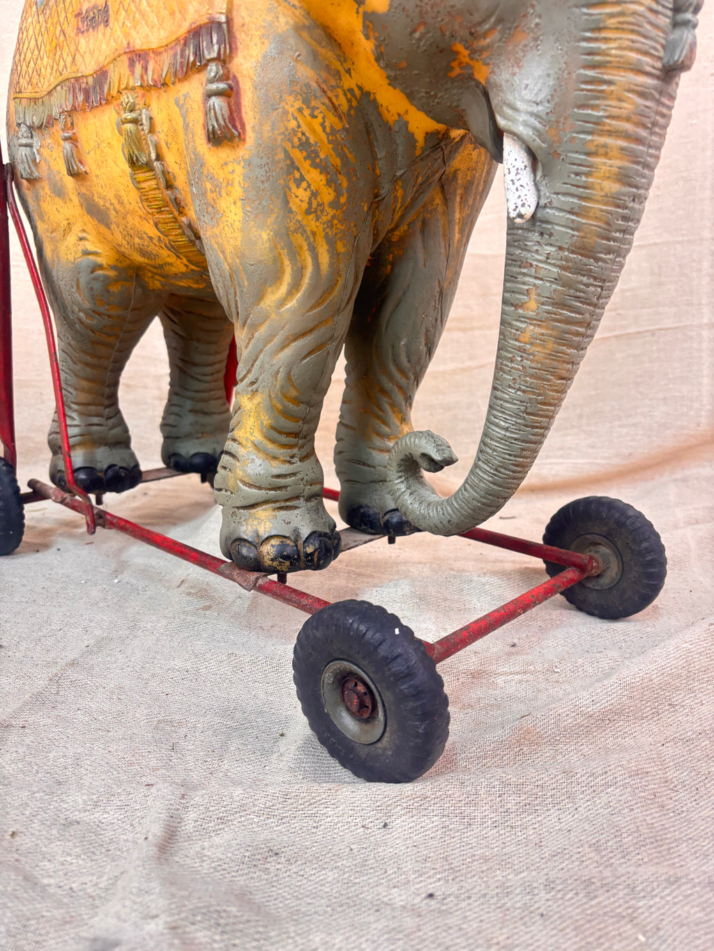 Vintage 1950s Tri-ang push-along elephant toy with hard plastic body, blue saddle, and red metal chassis with rubber wheels