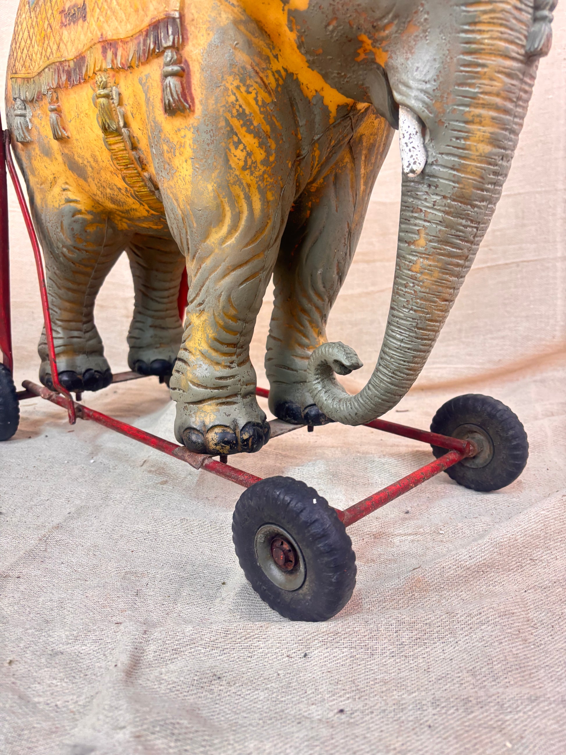Vintage 1950s Tri-ang push-along elephant toy with hard plastic body, blue saddle, and red metal chassis with rubber wheels