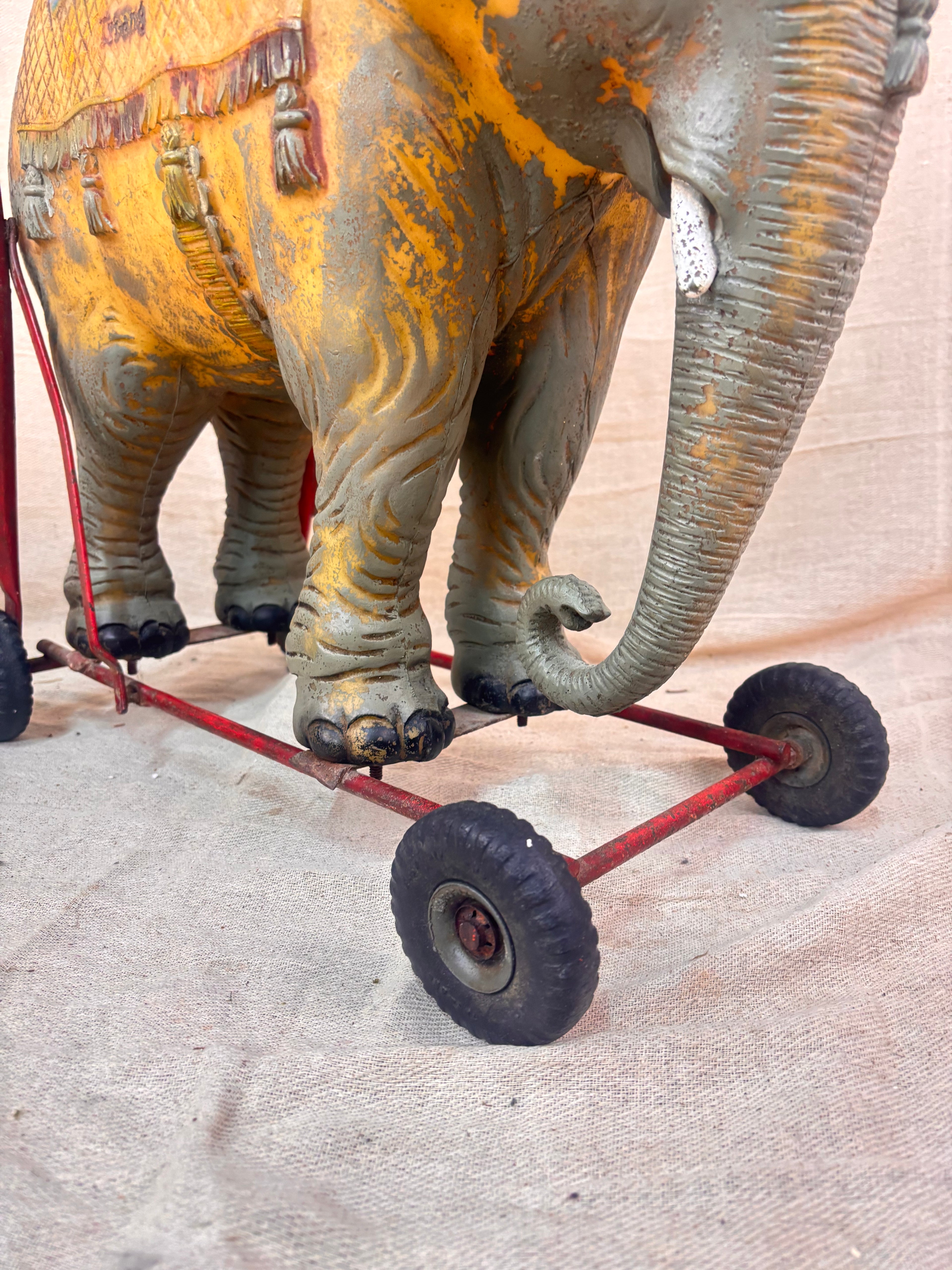 Vintage 1950s Tri-ang push-along elephant toy with hard plastic body, blue saddle, and red metal chassis with rubber wheels