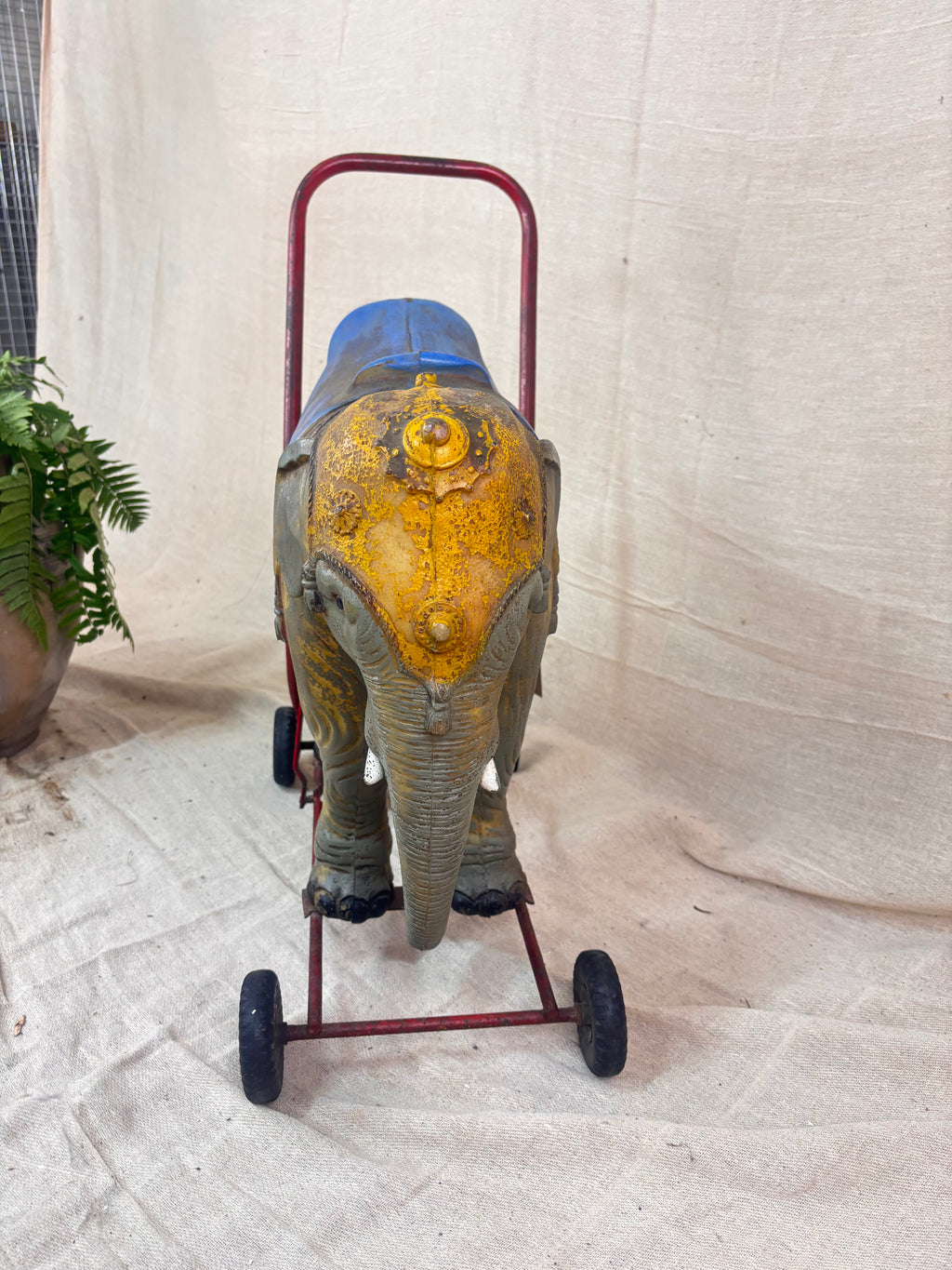 Vintage 1950s Tri-ang push-along elephant toy with hard plastic body, blue saddle, and red metal chassis with rubber wheels