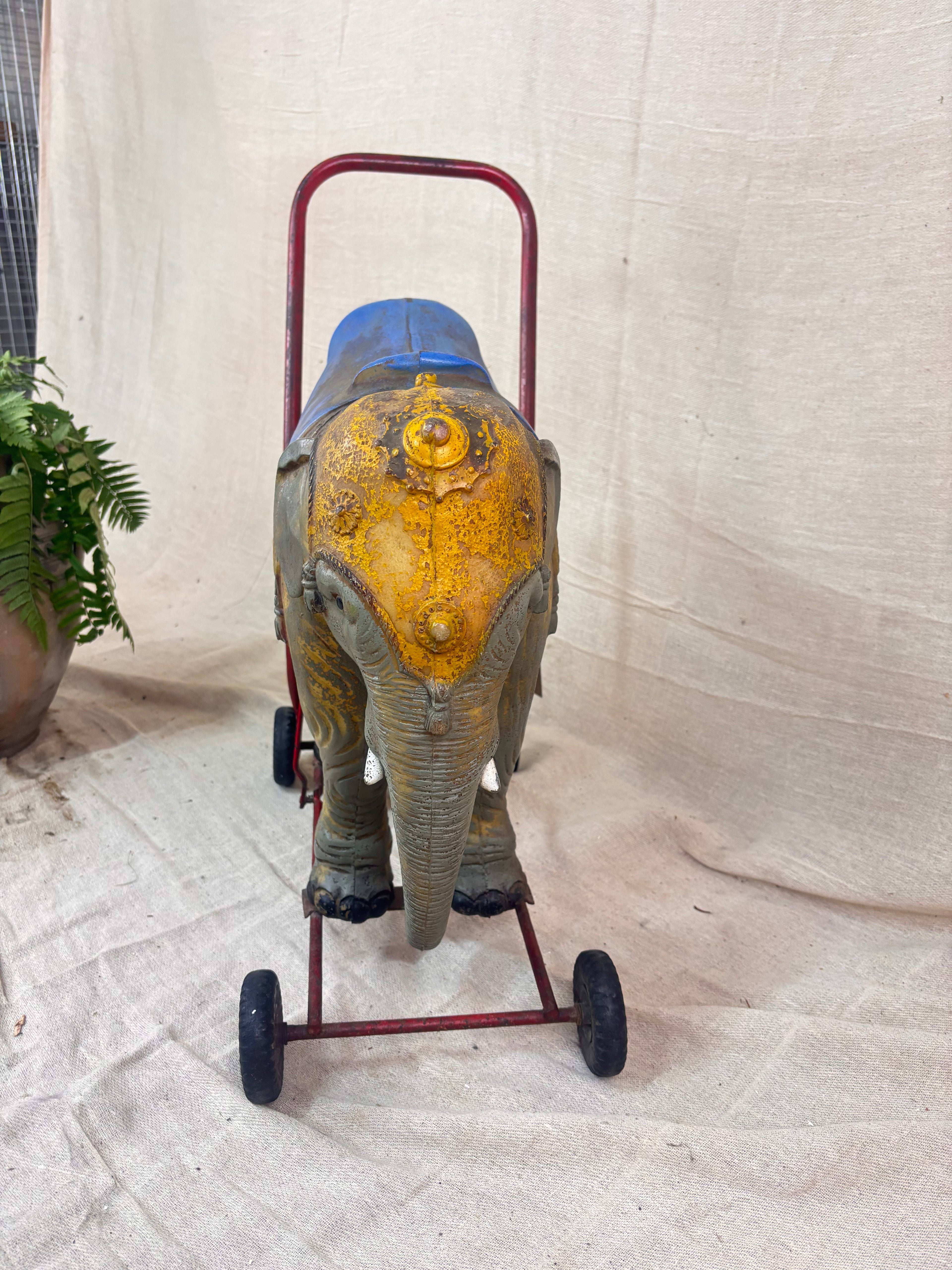 Vintage 1950s Tri-ang push-along elephant toy with hard plastic body, blue saddle, and red metal chassis with rubber wheels