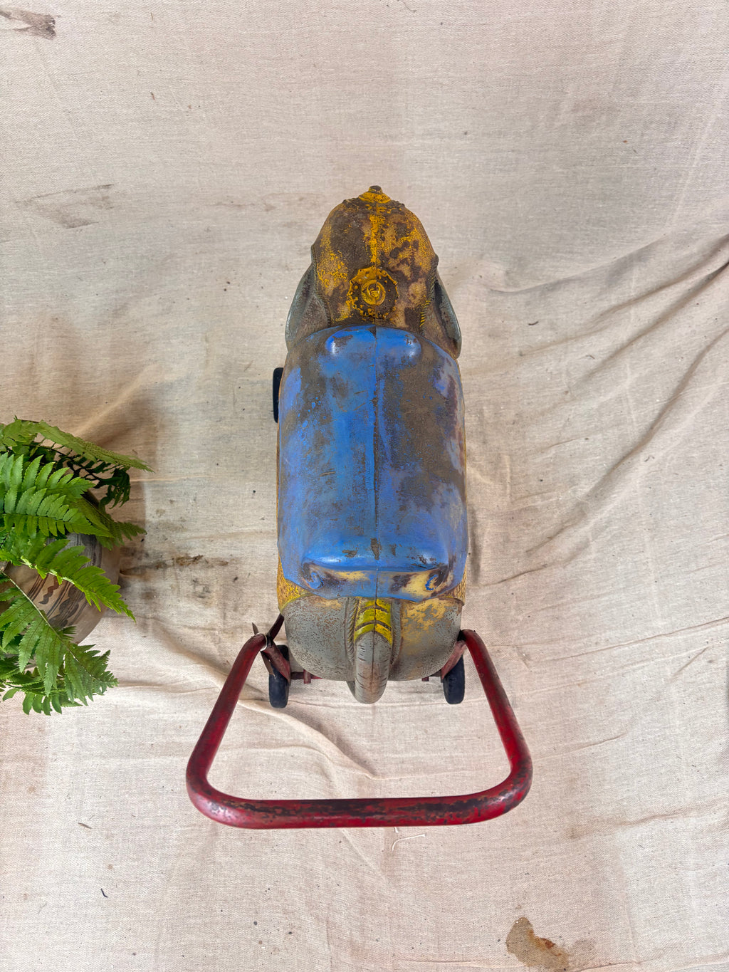 Vintage 1950s Tri-ang push-along elephant toy with hard plastic body, blue saddle, and red metal chassis with rubber wheels